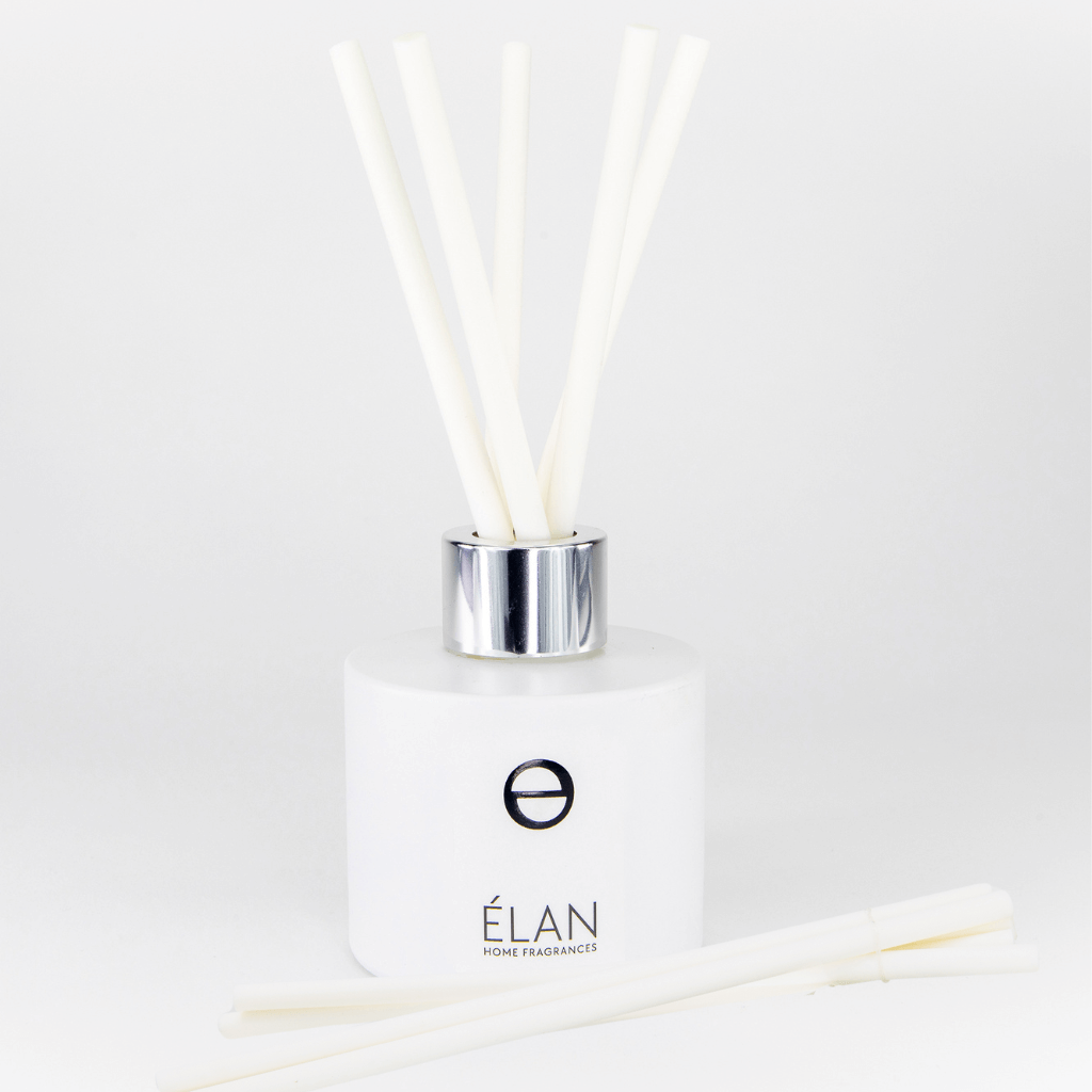 A set of white fibre reeds for a diffuser, displayed with a white square diffuser bottle and a silver cap, against a white background.