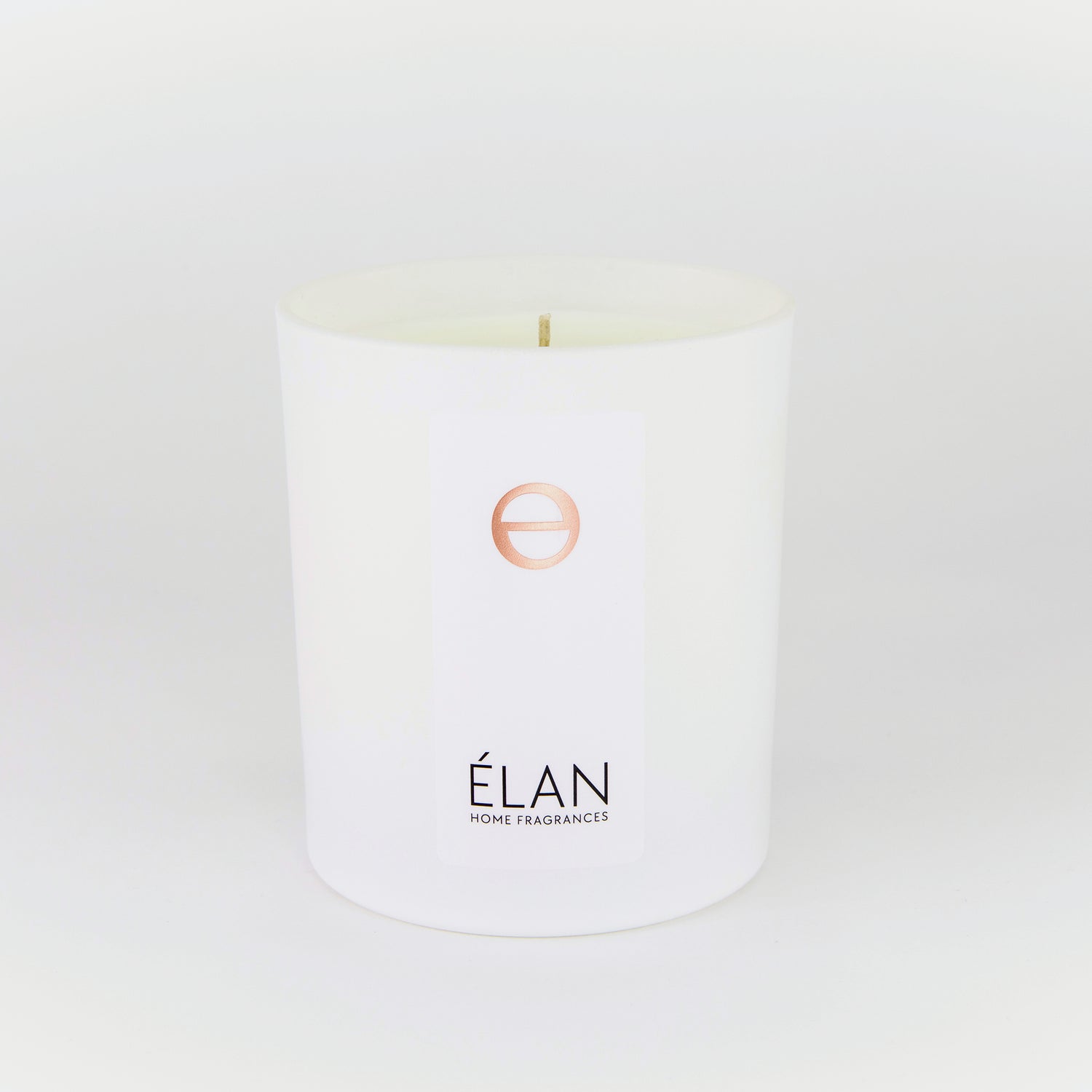 A white candle with a label that reads ÉLAN and has a design that resembles a flower.